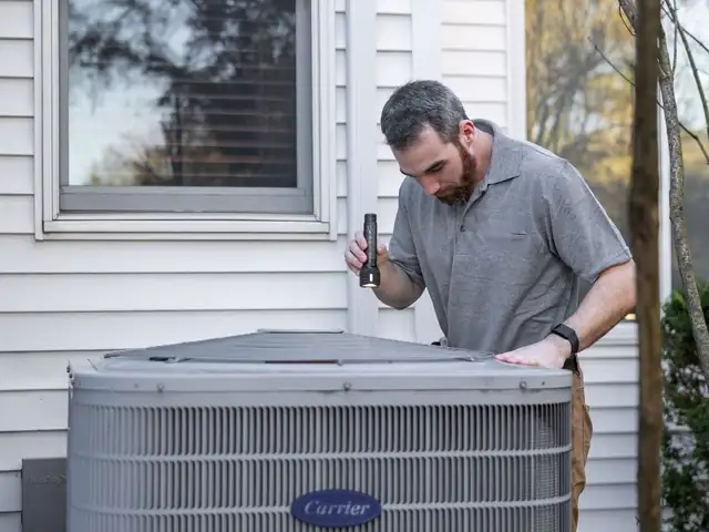 A technician kneeling beside an outdoor air conditioner.